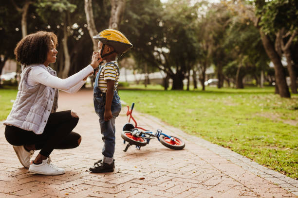 madre che aiuta il figlio a indossare il casco per andare in bicicletta - child assistance women family foto e immagini stock