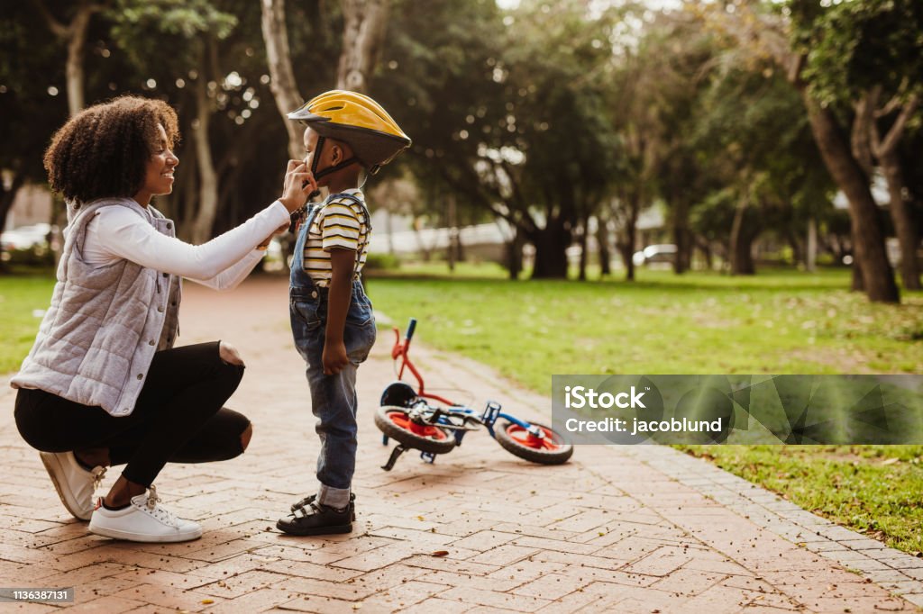 Mother helping son wearing helmet for cycling Mother helping son wearing helmet for cycling at park. Boy getting ready by wearing bike helmet to start cycling. Child Stock Photo