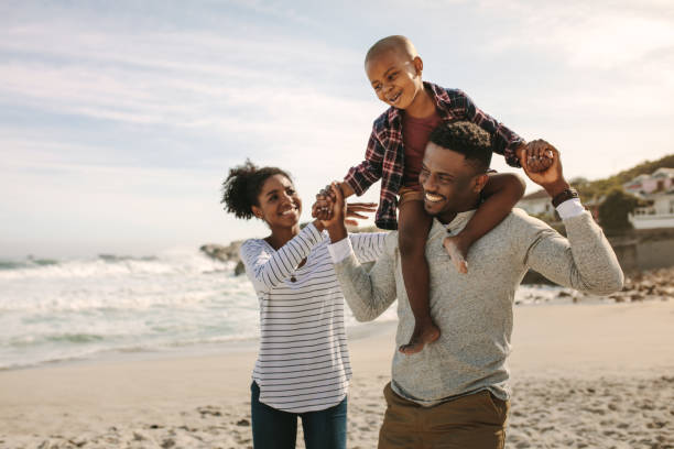 ouders dragen zoon op de schouders op het strand vakantie - family stockfoto's en -beelden