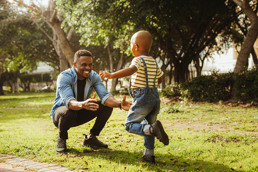 Cute son running into father's arms. Boy rushing into father's embrace at the park.