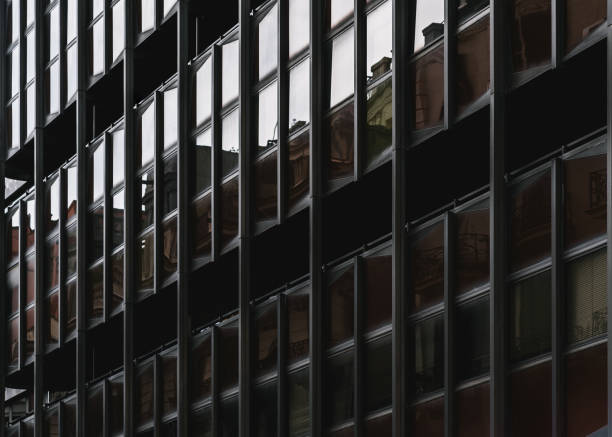 A dark atmospheric facade of an ordinary residential building with iron beams and windows of different types: brown, reflecting and transparent, two black gaps with balconies, Barcelona, Spain