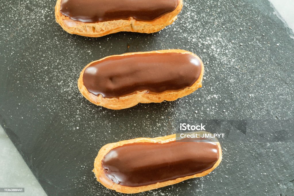 Traditional french pastry : aerial view of Eclair with chocolate icing Tree "eclair" with chocolate placed in a row on a slate powdered with powdered sugar. Aerial view Eclair Stock Photo