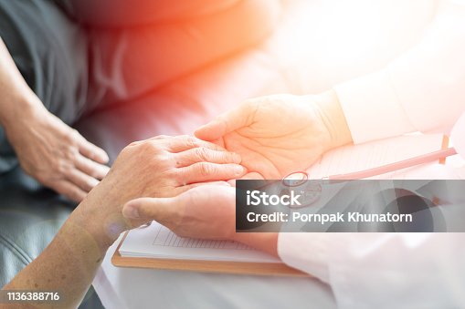 istock Parkinson and alzheimer female senior elderly patient with caregiver in hospice care. Old woman holding hand with doctor physician. 1136388716