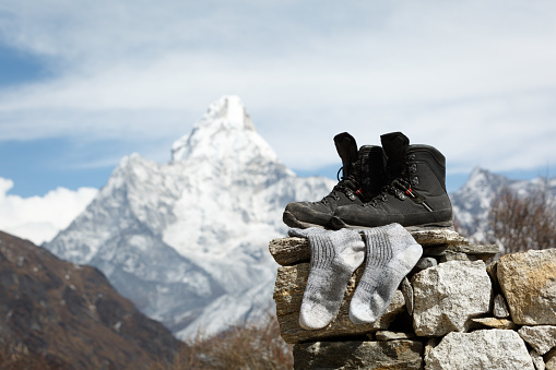 Hiking boots are dried on stones in sunny weather. Near trekking socks. Mount Ama Dablam is blurred. Everest Trail Base Camp