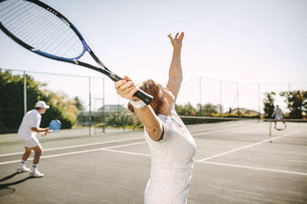 seniorenfrau, die beim tennisspielen einen service macht - tennis active seniors healthy lifestyle senior men stock-fotos und bilder