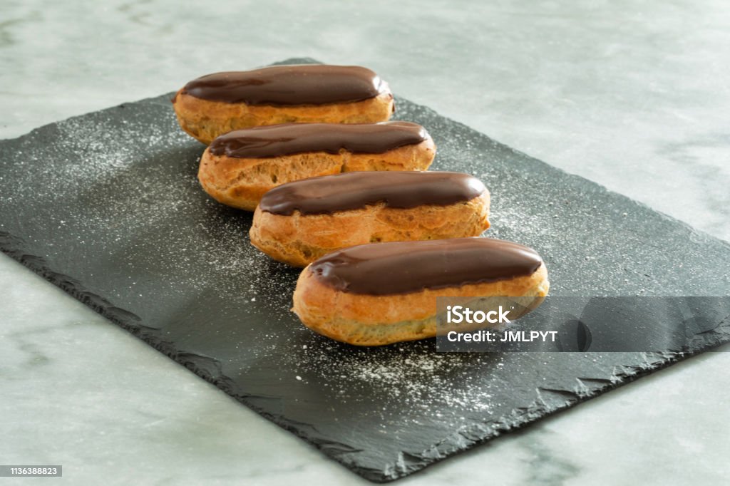 Traditional french pastry : Eclair with chocolate icing four "eclair" with chocolate placed in a row on a slate powdered with powdered sugar. Eclair Stock Photo