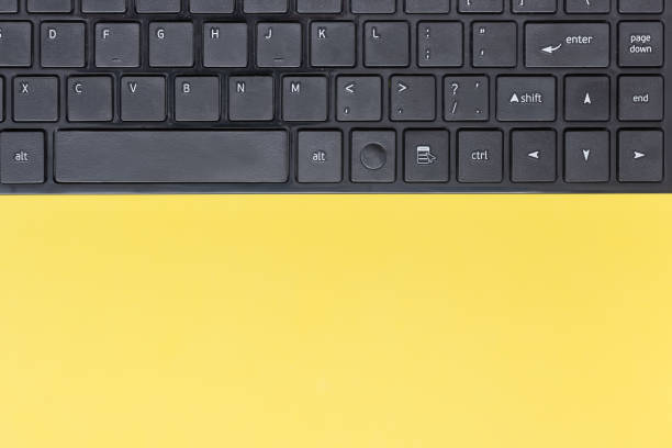 istock Black keyboard of a personal computer lying on a yellow paper background. Minimal creative concept 1136392097