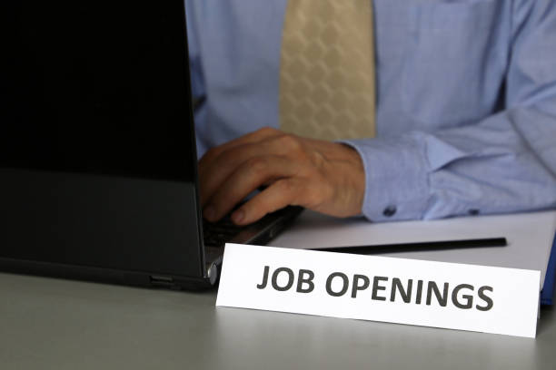 empregar e recrutar, homem na camisa azul e nos trabalhos do laço, sentando-se em uma tabela com o portátil perto do sinal com a inscrição vagas de emprego - shirt and tie typing communication part of - fotografias e filmes do acervo