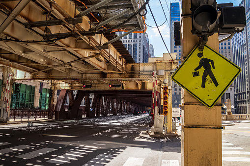 Wells Street view of pedestrian crossing amongst shadows cast from overhead elevated train tracks in Chicago, IL
