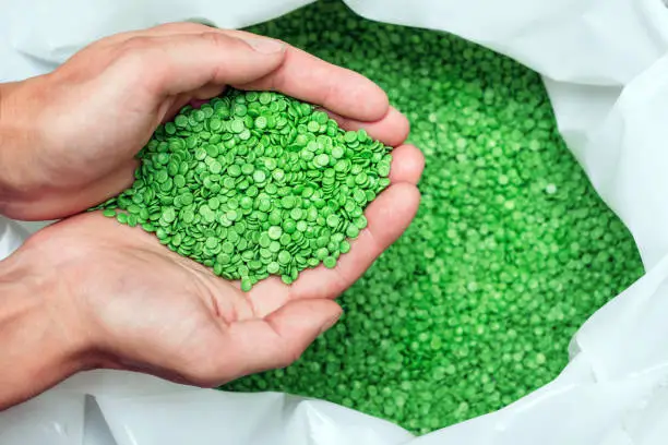 Photo of hands hold or touching biodegradable plastic pellets, plastic polymer granules