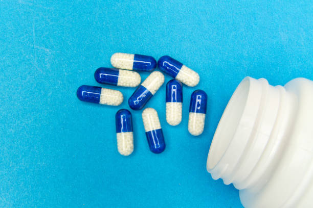 capsule (pillole) sono state versate da una bottiglia bianca su sfondo blu. background medico, modello. - diet pill foto e immagini stock