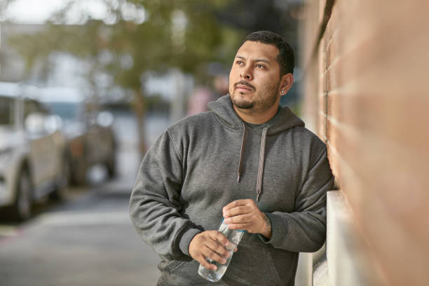 Thoughtful man holding water bottle leaning on wall