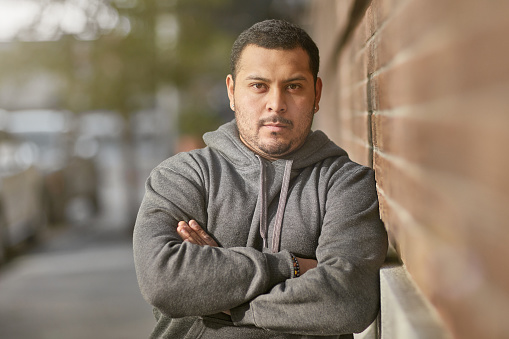 Portrait of young man with arms crossed leaning on brick wall. Confident man is in sportswear. He is resting after workout in city.