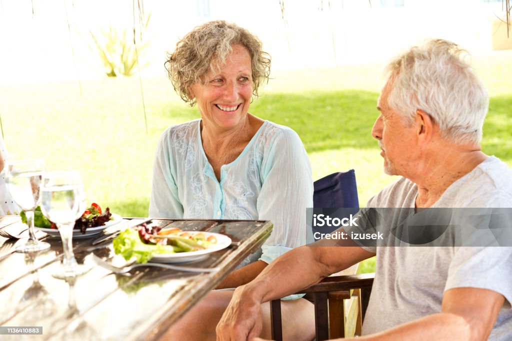 Smiling senior couple enjoying breakfast in resort Smiling senior couple talking while having breakfast. Elderly man and woman are sitting at table. They are enjoying vacation in resort. 60-64 Years Stock Photo