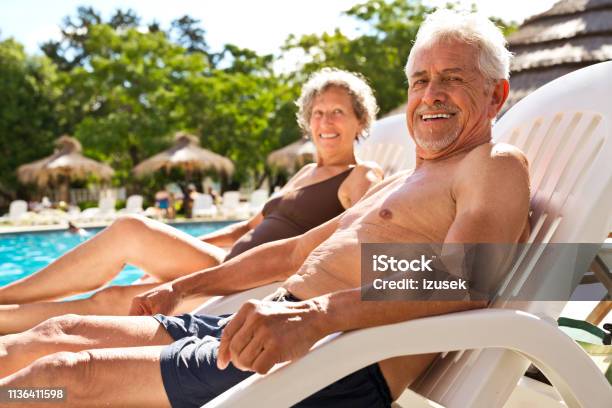 Retired Couple Resting On Deck Chairs At Poolside Stock Photo - Download Image Now - Swimming Pool, Senior Adult, Relaxation