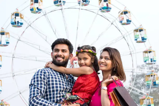 Happy Indian family with shopping bag in front of giant ferris wheel