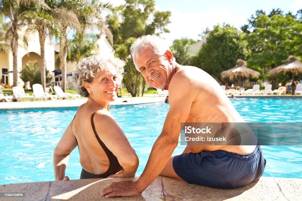 Portrait of smiling senior couple at poolside Portrait of smiling senior couple resting at poolside. Retired elderly male and female enjoying summer vacation. They are in swimwear. Senior Couple Stock Photo