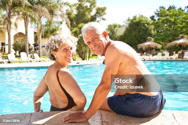Portrait Of Smiling Senior Couple At Poolside Stock Photo - Download Image Now - Senior Couple, Swimming Pool, 60-64 Years