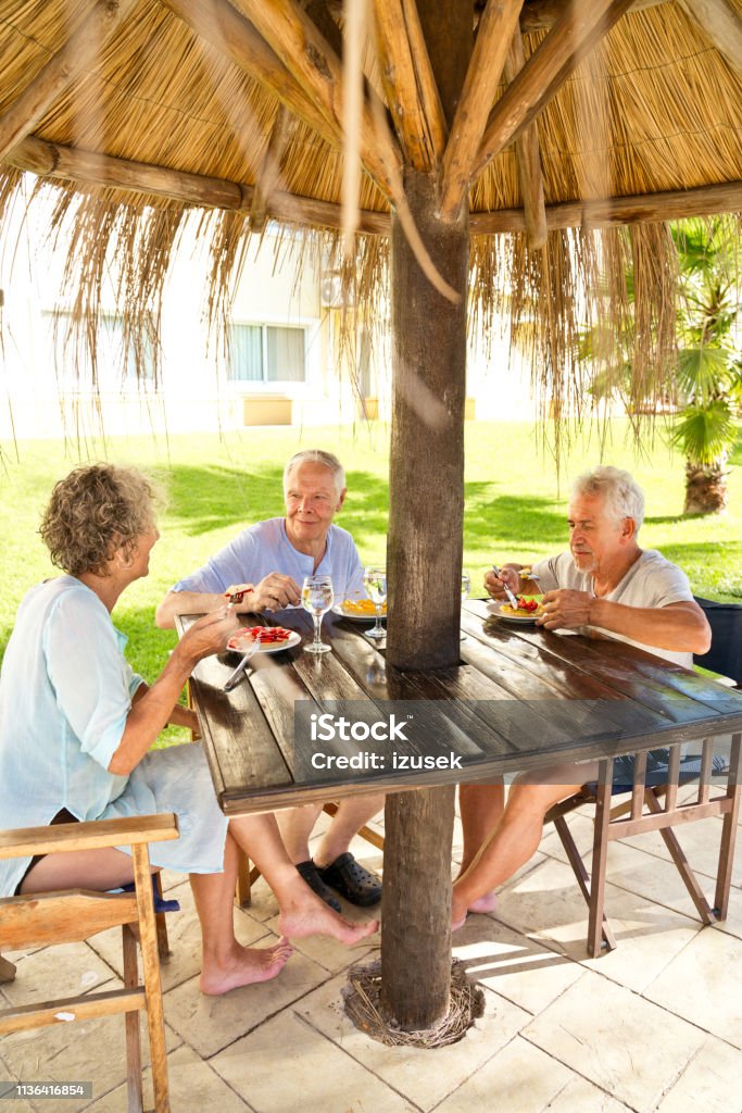 Senior friends enjoying breakfast in resort Senior friends enjoying breakfast at wooden table. Elderly men and woman are spending leisure time at resort. They are enjoying their retirement in vacation. 70-79 Years Stock Photo