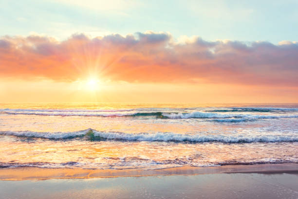 olas oceánicas en la playa al atardecer, rayos solares. - arena fotos fotografías e imágenes de stock