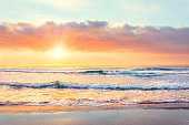 Ocean wave on the beach at sunset time, sun rays.