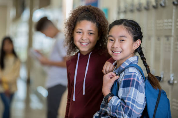 Diverse middle school girls smiling at camera in hallway near lockers before class