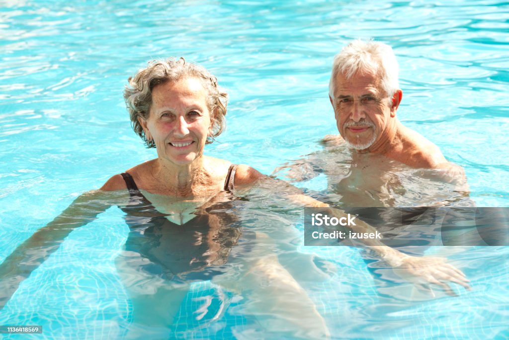 Portrait of happy senior couple swimming in pool Portrait of senior couple swimming in pool. Retired elderly man and woman are enjoying in water. They are having fun in vacation. Senior Adult Stock Photo