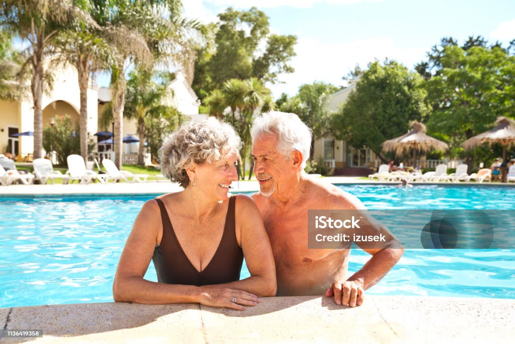 Smiling senior couple looking at each other Smiling retired couple looking at each other. Senior man and woman enjoying in swimming pool. They are spending leisure time during vacation. Senior Couple Stock Photo