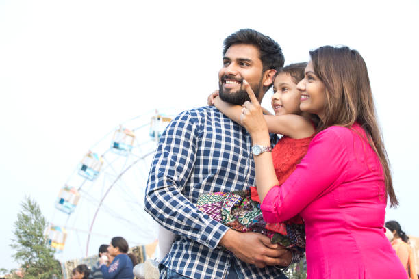 Happy family standing in front of ferris wheel Happy family standing in front of ferris wheel happy indian young family couple stock pictures, royalty-free photos & images
