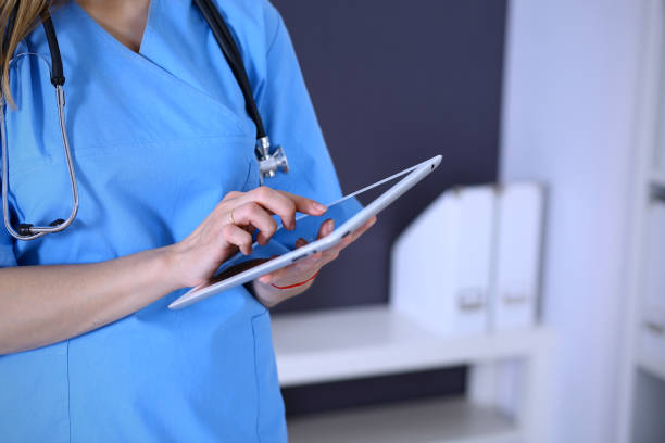 istock Woman doctor using tablet computer while standing straight in hospital office, closeup. Healthcare, insurance and medicine concept. 1136432874