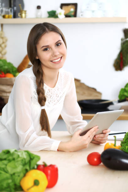 istock Young  woman using tablet while cooking or making online shopping in kitchen. Girl looking at the camera. Healthy lifestyle and vegan meal concepts 1136432979