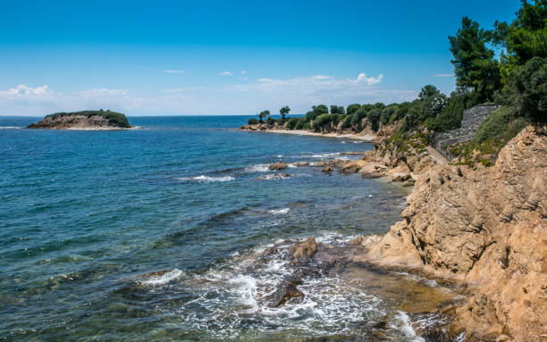 Beautiful idyllic seascape with a view on the coastline, blue water and little island. A little peninsula and rocky coastline with Mediterranean trees and plants and little island in the distance surrounded by turquoise and blue sea on the beautiful summer day. ivory coast landscape stock pictures, royalty-free photos & images