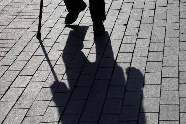 istock Silhouette of man walking with a cane, long shadow on pavement 1136433422
