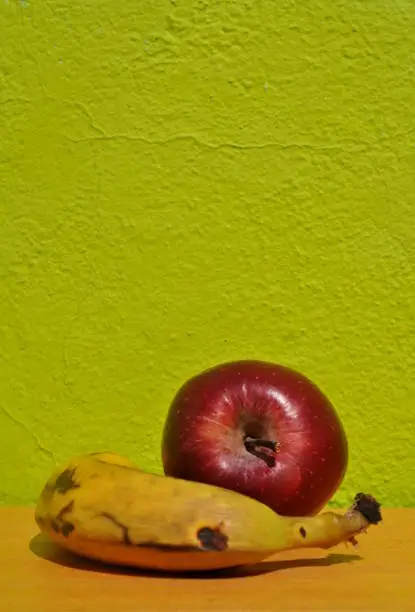 Red apple and old banana in a kitchen with green lime background