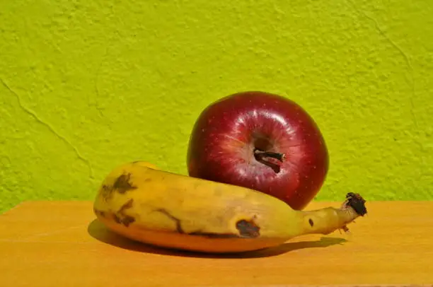 Red apple and old banana in a kitchen with green lime background