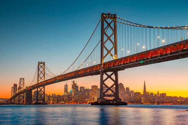 San Francisco skyline with Oakland Bay Bridge at sunset, California, USA Classic panoramic view of San Francisco skyline with famous Oakland Bay Bridge illuminated in beautiful golden evening light at sunset in summer, San Francisco Bay Area, California, USA bridge built structure stock pictures, royalty-free photos & images