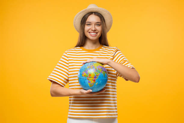 istock Young smiling girl holding globe with both hands, isolated on yellow background 1136438184