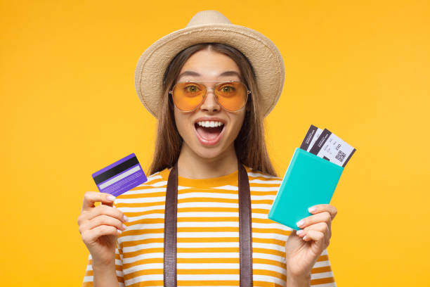 Excited young female tourist holding credit card and passport with tickets, ready to flight, isolated on yellow background Excited young female tourist holding credit card and passport with tickets, ready to flight, isolated on yellow background airplane ticket photos stock pictures, royalty-free photos & images