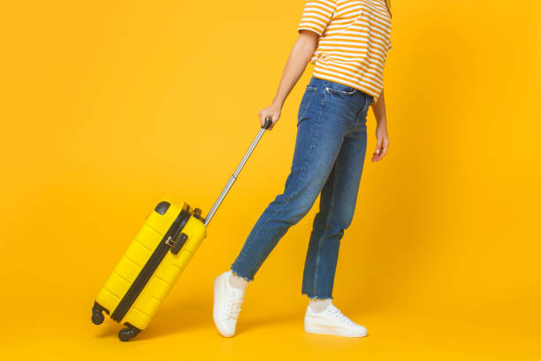 travel and tourism concept. young woman wearing casual clothes walking with suitcase isolated on yellow background - shoe leaving women summer imagens e fotografias de stock