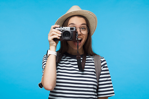Smiling young girl tourist holding camera, isolated on blue background