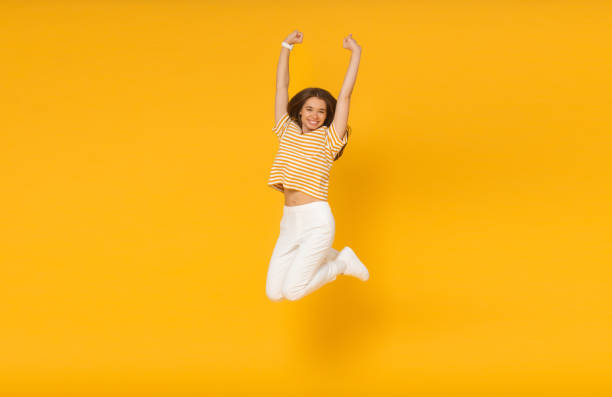 fröhlich fröhliches mädchen springt in die luft mit erhobenen fäusten, wenn sie siegerin ist, auf gelbem hintergrund isoliert - fashion model beautiful power action stock-fotos und bilder