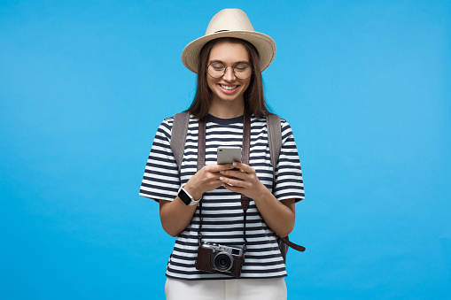 Happy smiling young woman tourist holding smartphone, using online map app or booking flight tickets, isolated on blue background