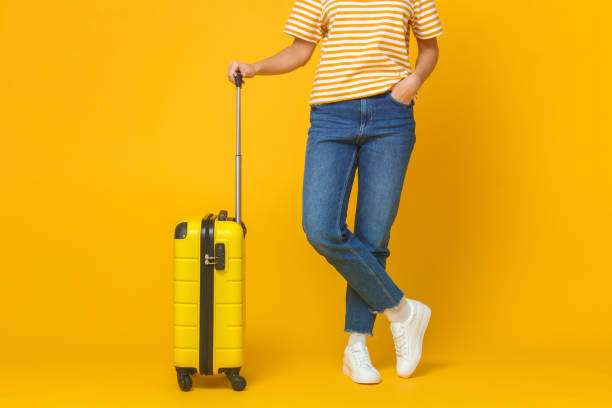 travel and tourism concept. young woman wearing casual clothes holding suitcase isolated on yellow background - shoe leaving women summer imagens e fotografias de stock