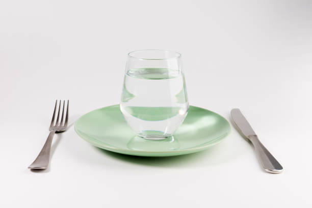 glass of water in a plate with knife and fork isolated on white background stock photo
