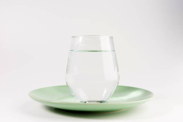 glass of water in a plate isolated on white background stock photo