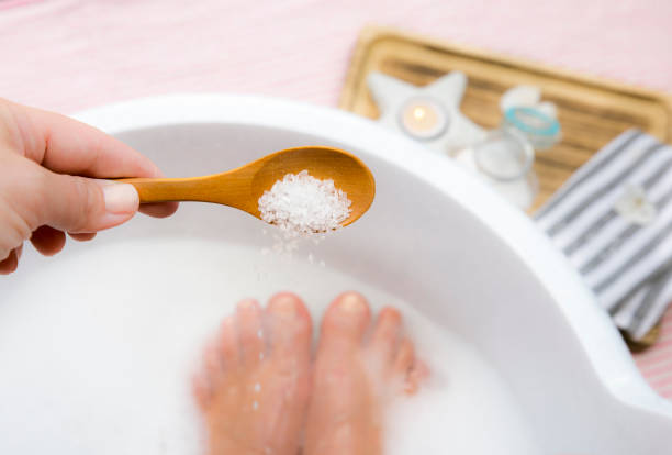 Adding Magnesium Chloride vitamin salt in foot bath water, solution. Magnesium grains in foot bath water are ideal for replenishing the body with this essential mineral, promoting overall wellbeing. stock photo