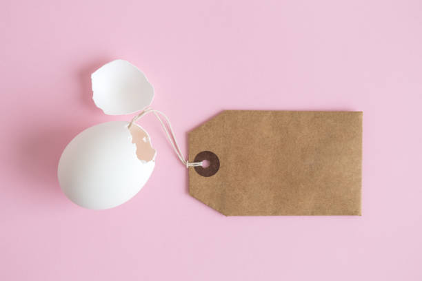 Flat lay of white cracked eggshell with price tag abstract on pastel pink background. Egg shell with blank price tag minimal easter shopping creative concept. conceptual realism stock pictures, royalty-free photos & images