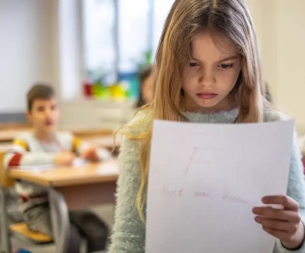 Cute little girl looking at paper with F grade and she are sad