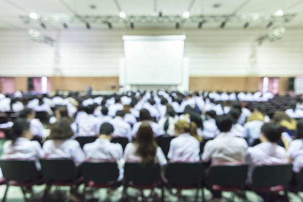 istock Blurred abstract background of educational conference in auditorium hall with students sitting in seat rows and presenters on stage 1136476854