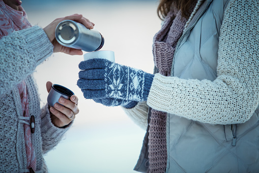 Midsection of two women having coffee from a vacuum flask to warm up on a winter day.